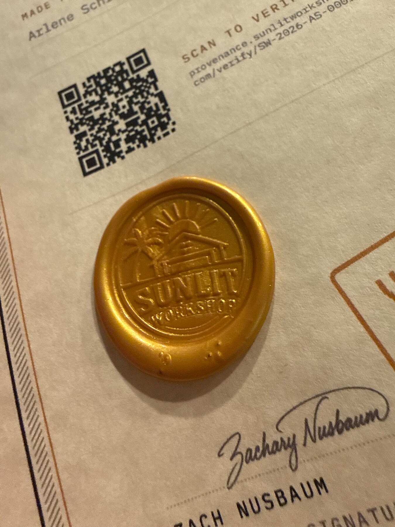 A custom brass Sunlit Workshop stamper pressed into a gold wax seal beside its QR code and certificate